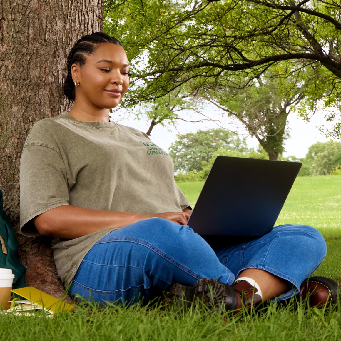 A young woman sitting under a tree working on a laptop